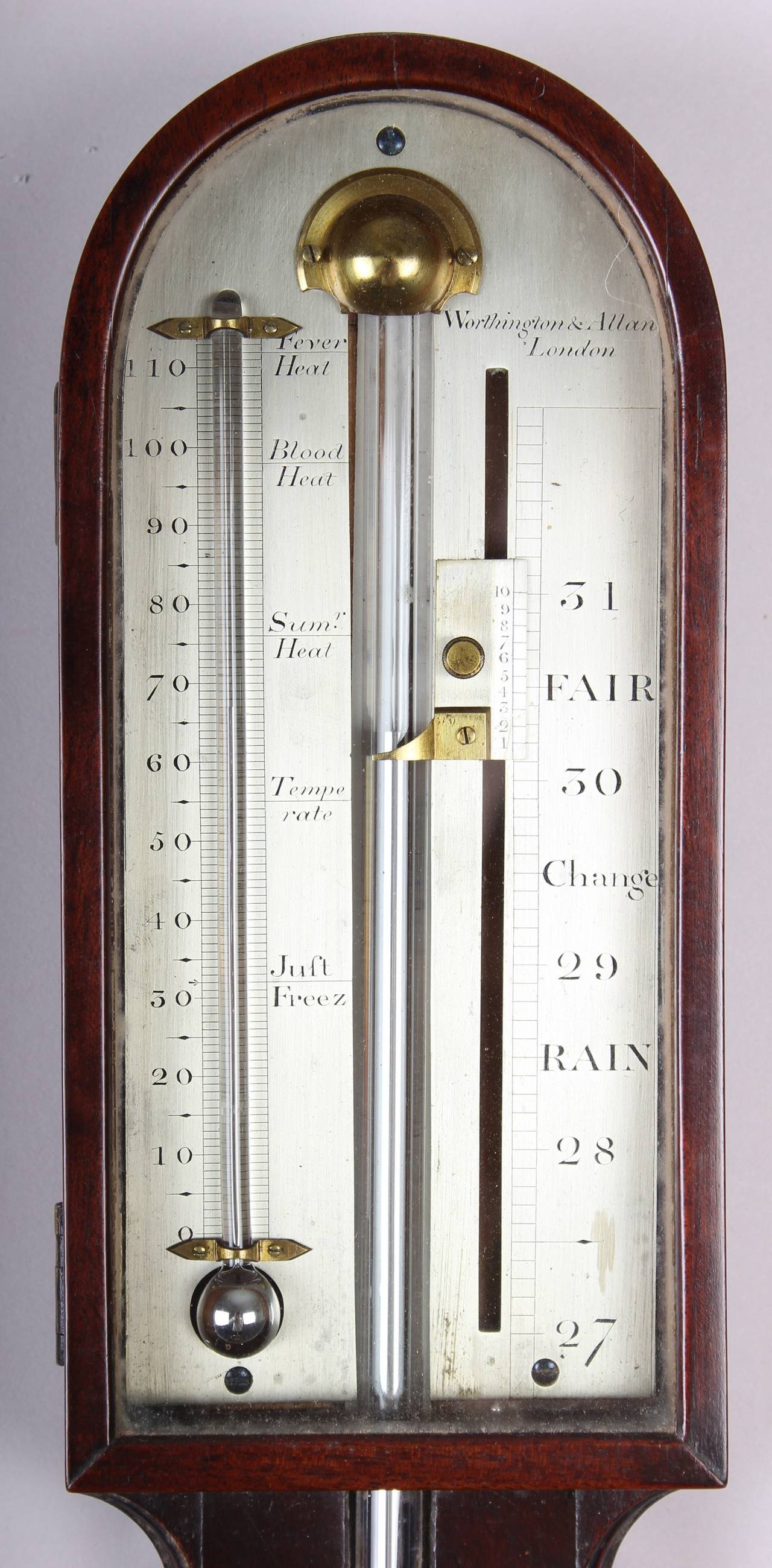 Early 19th century mahogany stick barometer by Worthington & Allan, London; the enclosed arched and silvered register fitted with a thermometer; the richly-coloured case with a chevron veneered ground and a hemi-spherical cistern-cover.