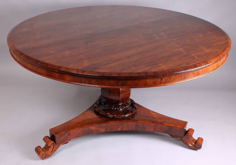 William IV period rosewood circular centre dining table; the hinged circular top of richly colored matched veneers, on an octagonal baluster shaft with a stylized lotus and rope-twist collar, on a triangular concave-sided platform with scrolled