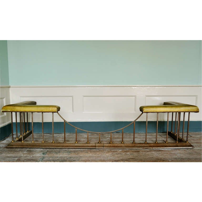 A large steel and brass club fender, upholstered with green leather on moulded plinth base.

Available to view at Brunswick House, London.