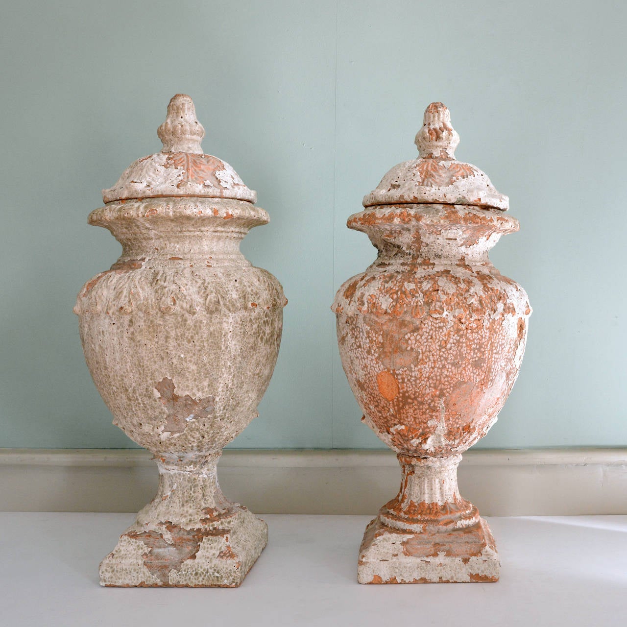A pair of Italianate terracotta lidded urns, the lids and bulbous bodies decorated with stiff leaf motif, the waisted socle on square plinth base. Distressed majolica glaze all over, one urn repaired (socle).

Available to view at Brunswick House,