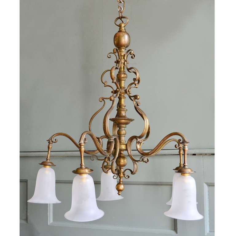 An English five-arm brass chandelier, early 20th Century, in the Art Nouveau taste,the stem with baluster mouldings, suspended on a ball and loop, each scrolled arm with sinuously wrought supporting bracket, and milk-glass shade with everted