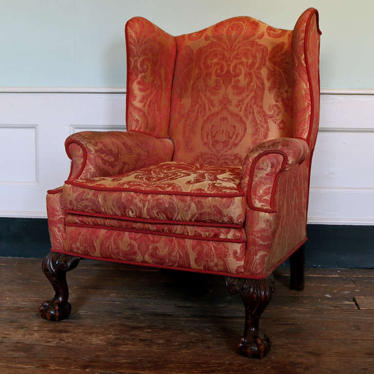 A late-19th century upholstered and mahogany wingback armchair, with shaped back and sides, scrolled arms and squab cushion, on acanthus-carved cabriole front legs with claw and ball feet.

Available to view at Brunswick House, London.