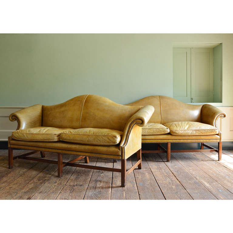 A pair of mahogany hump back sofas, in the George III style, upholstered in leather with squab cushions on moulded legs joined by stretchers.

Available to view at Brunswick House, London.