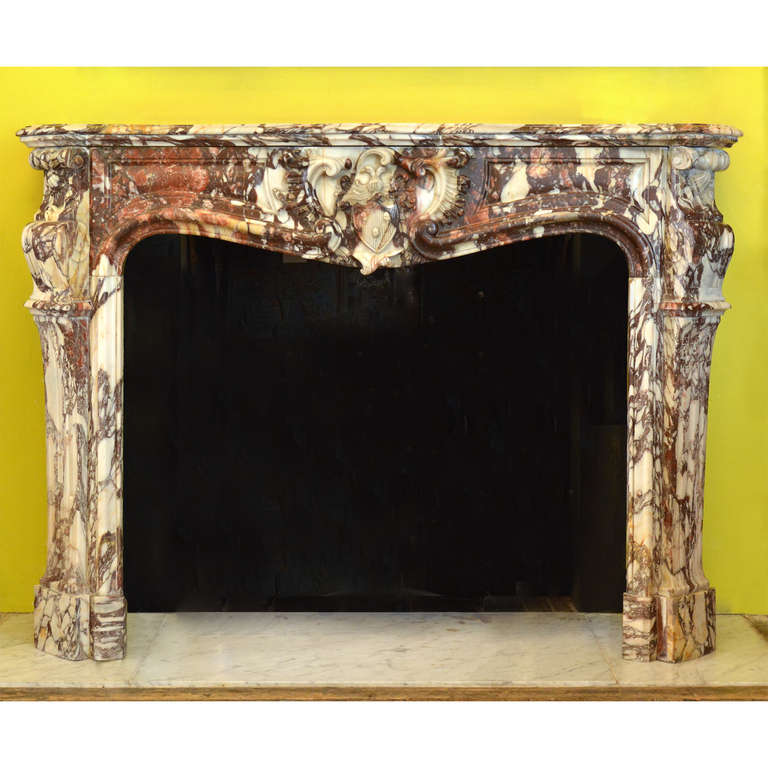 A Louis XVI style Breche de Medici marble chimneypiece,nineteenth century, French, the serpentine fronted shelf with shaped sides leading to serpentine frieze centred by highly decorative carved cartouche fielding a coat of arms comprising of