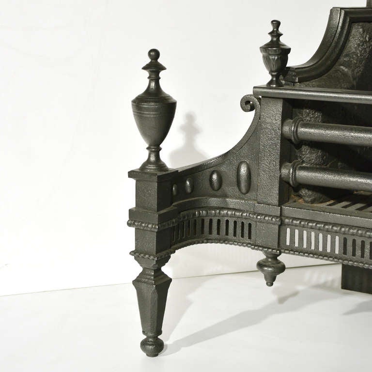 A large Regency cast iron and steel fire basket, of large proportions, the stylised sun burst shaped back-plate leading to shaped sides, with large front bars flanked by finial urns, the shaped pierced fretwork on square tapered supports topped with