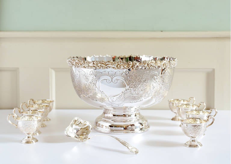 A substantial George III style silver-plated punch bowl, complete with eight decorative cups and ladle, the bowl with shaped and highly decorative rim incorporating cornucopia shells and stylized grapes leading to bulbous main body embossed and