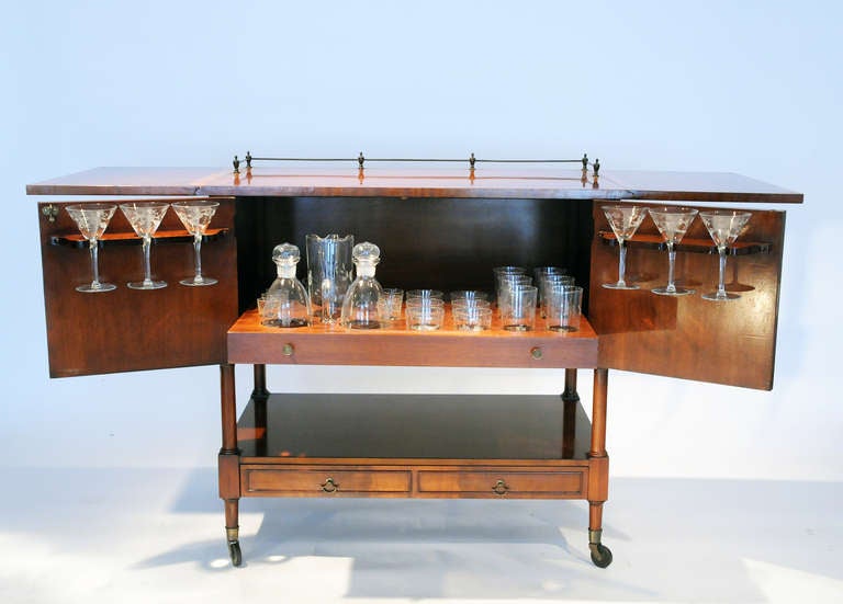 American two-door bar on casters with a complete set of six highball and six rock glasses, a glass ice bucket, martini glasses, two decanters, one pitcher, glass tray and glass swizzle stick. Made of mahogany with exotic wood inlay.