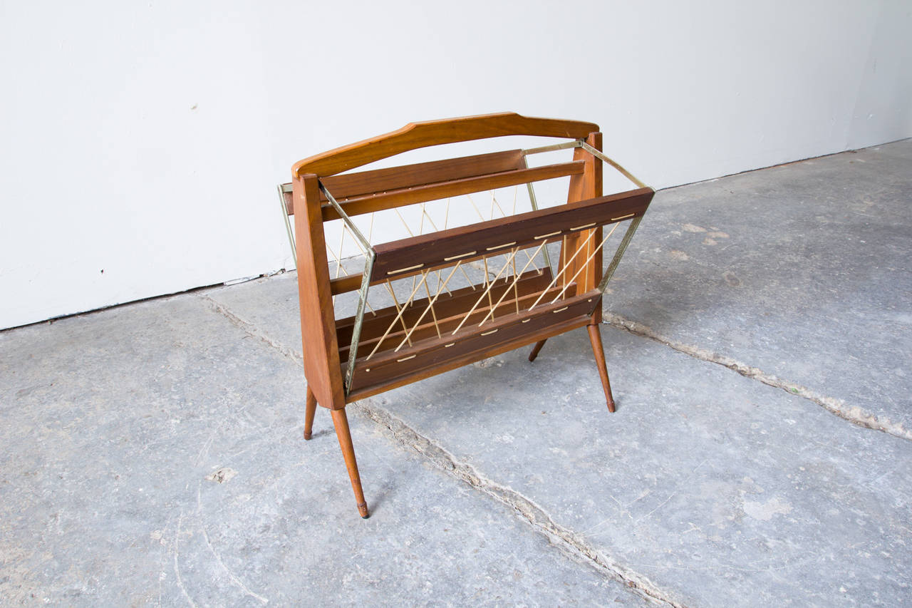An elegant and functional Italian magazine rack in wood, brass and rope. When lifted by the handle, the hardware pulls up the splayed sides, flattening the piece for easy transport or storage. Woven rope provides the support for papers and magazines