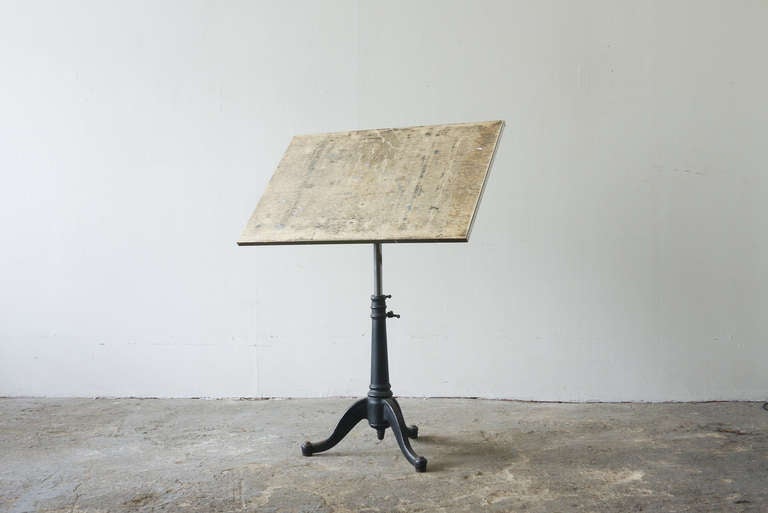 This drafting table is wood, with steel edging, and sits on a cast iron pedestal base with three legs. It tilts and swivels, and also adjusts in height from 30