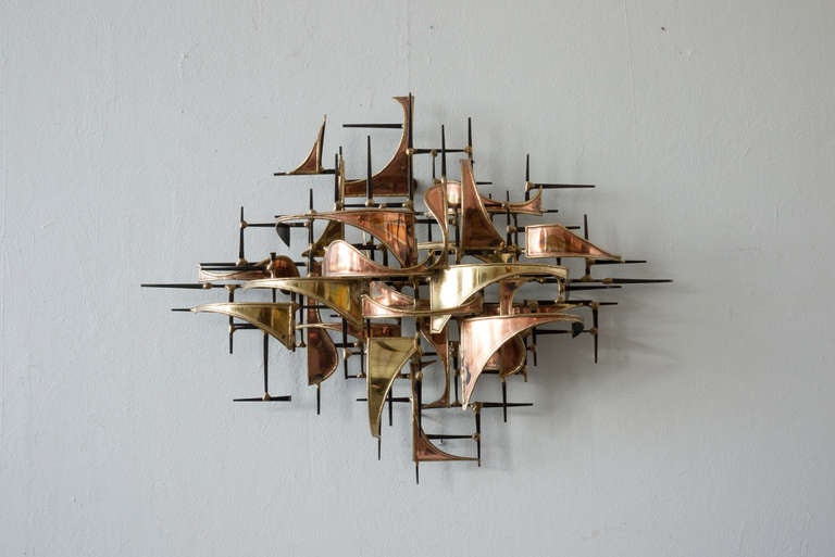 This brass/copper wall hung sculpture by Higgins features a brutalist aesthetic. The structure is composed of thin rod pieces of metal. Thin, ribbon like two-tone bent pieces make up the facade. It is signed and dated.