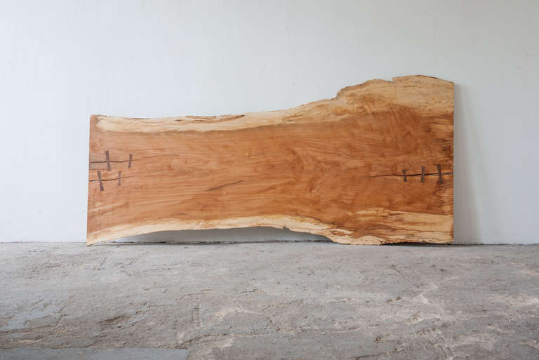This headboard, of beech wood has been as closely kept in its natural state as possible. The splits are secured by walnut butterflies. It was prepared and finished in the same process used by Nakashima. The headboard mounts to the wall by a french