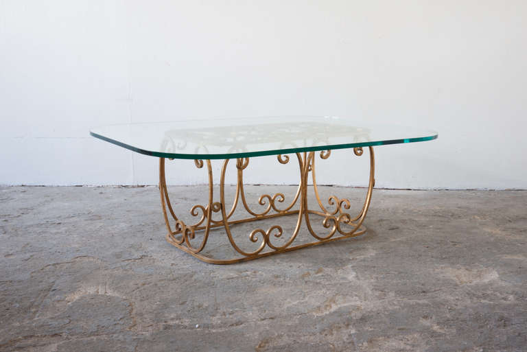 This decorative rectangular cocktail table features a gilded iron base, which supports a three quarter inch rounded rectangular glass top. It is light and airy and very sturdy.