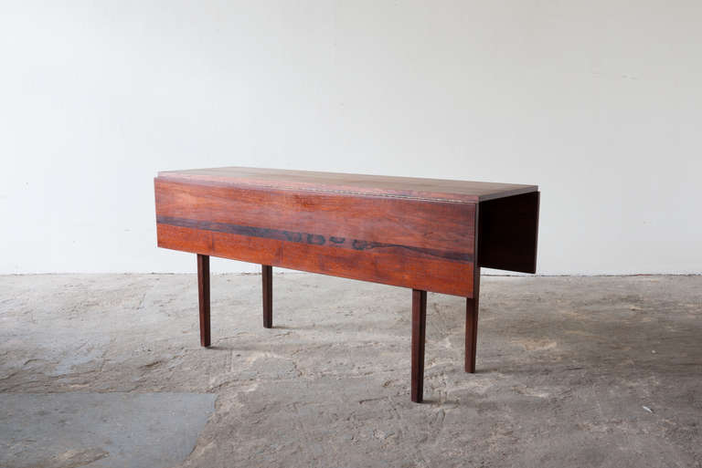 This drop-leaf table of walnut features elegant thin strips of rosewood inlay. The two leaves are supported by sliding rails beneath, and fold down on piano hinges. The legs are squared and tapered. 

Leaves up: 42