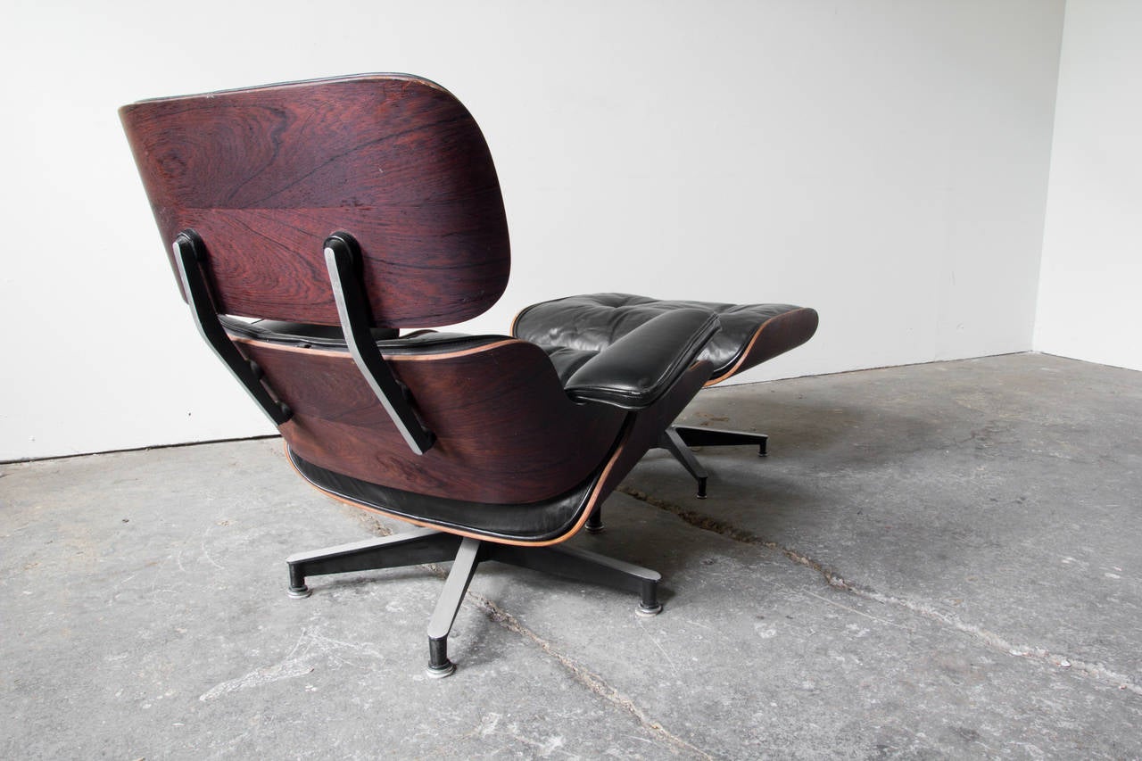 A fantastic second generation 670 lounge and 671 footstool by Charles and Ray Eames. Highly figural rosewood shells encase the original black leather upholstery. The lounge swivels on a five point aluminum base. The feet of the footstool's base
