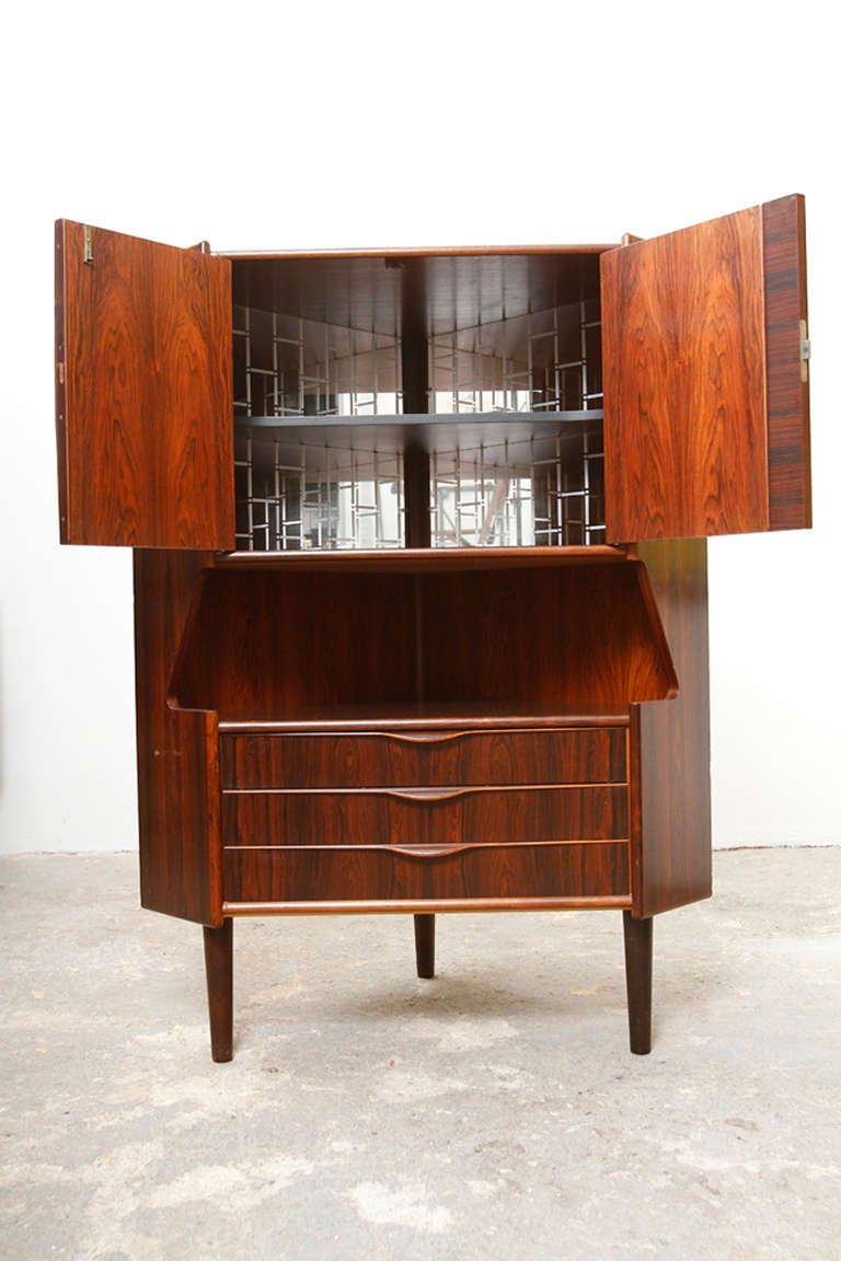 A rosewood corner cabinet designed by Gunni Omann for Omann Jun Mobelfabrik. It has three felt-lined bottom drawers and 2 locking cabinet doors above (key included).