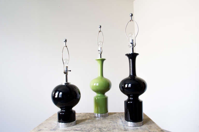 A group of mod, bulbous ceramic lamps, with chromed metal bases. One black lamp and a green lamp (only 2 left) make up the set. Each has a matching and complimentary finial, also of chrome, calling into context the base.

Tall Black:
Height –