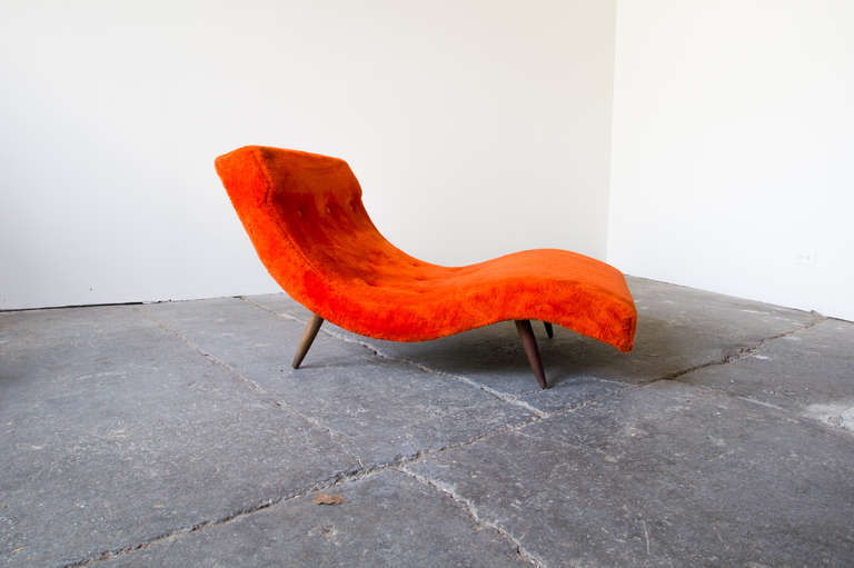 An organic form chaise lounge on tapered walnut legs by Adrian Pearsall for Craft Associates. This piece features its original buttoned upholstery, in a bright orange/red. The foam is thicker toward the headrest, making for a supportive and