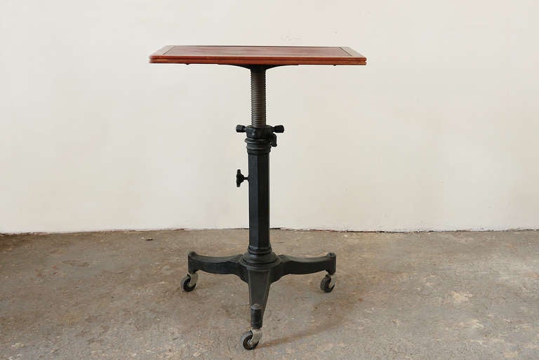 An adjustable antique table designed for an optometrist's office. Walnut tabletop with a vinyl inlay set on a steel base with wheels. The top adjusts from 26