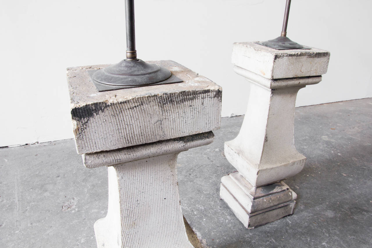A pair of architectural pedestals in cement, modified into lamps. Each has a long brass rod which run to double sockets with individual pull chains. The pedestals are tall and robust with attractive distressing and a desirable patina.