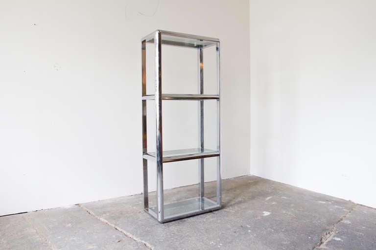 A simple and elegant etagere shelving unit with four glass shelves supported by a chromed steel frame. The shelves are equally spaced in thirds, with a shelf at the bottom and the top. The glass slides out easily for cleaning.