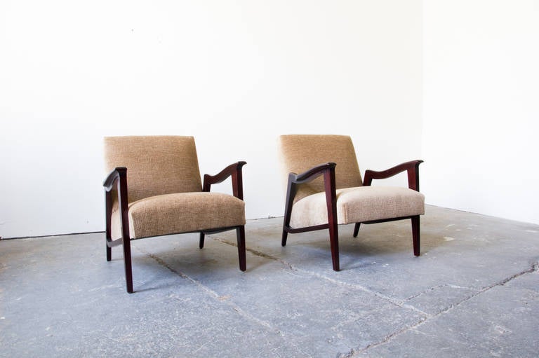 This outstanding pair of lounge chairs feature design idioms from Art Deco and Modernism. They are low and angle upward; overstuffed beige cushions bolden the solid, angular arms and legs. They are robust in appearance and structure– making for