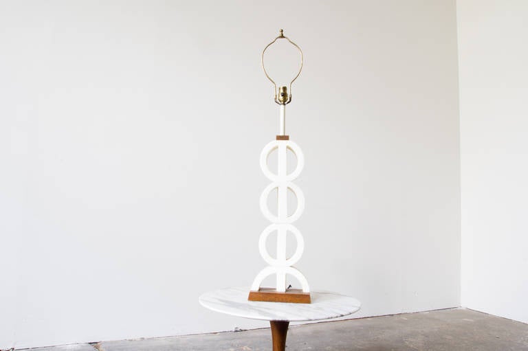 This table lamp, comprised of simple eyelet decoration in marble, stands on a wood base. At the top, before the stem, a proportional divider of wood caps off the body and calls back to the base. It stands tall but maintains a slim and airy profile.