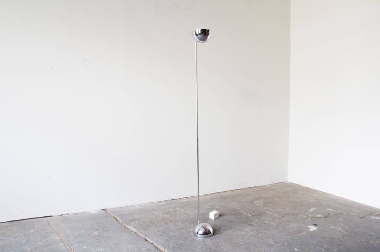 A polished-chrome floor lamp by George Kovacs with a weighted semi-sphere at the base, which gives way to a long thin stem. The shade is proportionate to the base, and directs light upward for soft, bounced light.