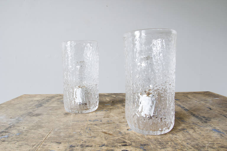 A pair of hand blown-glass table lamps. The porcelain housing is mounted at the bottom of the glass. The texture of the glass dapples the light in a pleasing manner, and adds a candle-like warmth the the glow.