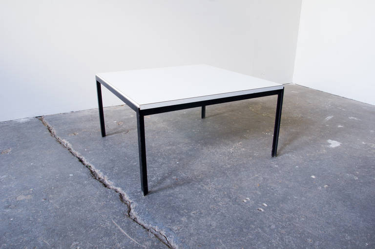 A square coffee table by Florence Knoll. The blackened steel frame does much to accentuate the stark, white laminate surface. This table is small-sized, elegant, and built to last.
