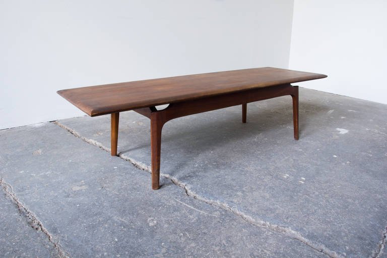 A long Danish influenced surfboard coffee table in walnut. The surface is of solid wood board construction. Chamfered edges, legs and rails create a sculptural effect. The floating surface design adds a feeling of airiness to an otherwise robust