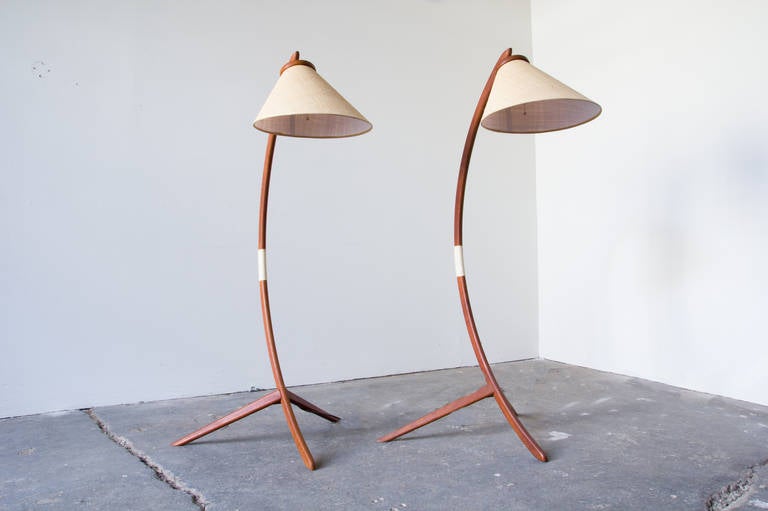 A stunning pair of Danish floor lamps in teak. The third leg of the tripod base carries up through the design and forms the bowed support to which the shade is attached. A wrapped string around the middle functions both as a handle and to conceal