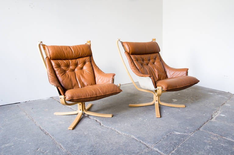 A pair of falcon chairs by Sigurd Ressel for Vatne Møbler. Bentwood maple comprises the frame, which suspends a canvas sling. The sling is covered in the original caramel leather. Each piece retains its label.
