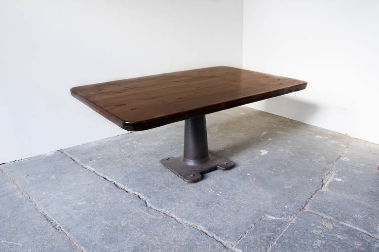 A dining table of solid, reclaimed, wood board construction on an iron pedestal machine base. The pedestal allows for spaciousness, and a feeling of airiness to an otherwise robust aesthetic.