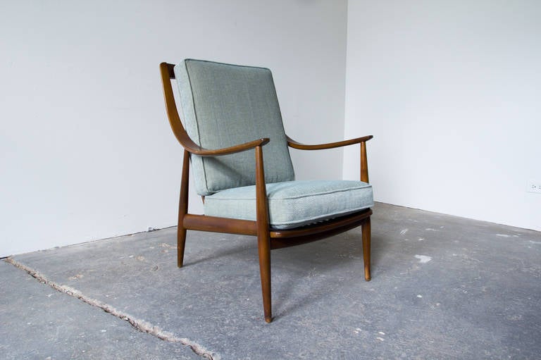 An easy chair by Peter Hvidt and Orla Mølgaard Nielsen, fabricated by France & Daverkosen. Curved arms, which begin at the top of the tall frame, swoop down through the profile of the chair. Tapered legs begin at the armrests, subtly thicken and