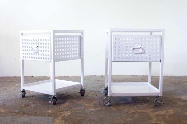 These side tables on castors, of painted steel, feature a single ventilated drawer and a shelf beneath. Though substantial in structure, their presence is light and airy.