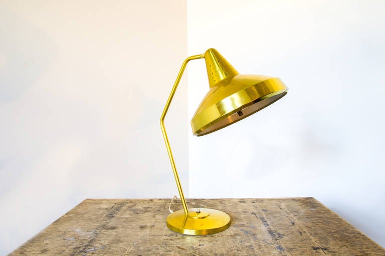 A brass desk lamp by Bill Scarlet or Swivelier. The lamp head is attached to the stem via a ball and socket joint, allowing for an array of positioning choices. The bend of the stem does well to accommodate the shape of the shade in its default