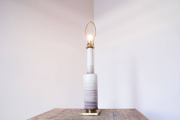 A tall bottle form glossy ceramic Stiffel lamp with a square brass base. It is well constructed, sturdy, and thoughtfully designed. The body features subtle violet stripes at varying distances.