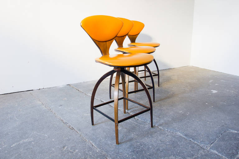 A set of three bent plywood and orange vinyl swivel stools by Norman Cherner for Plycraft. Like his famous 