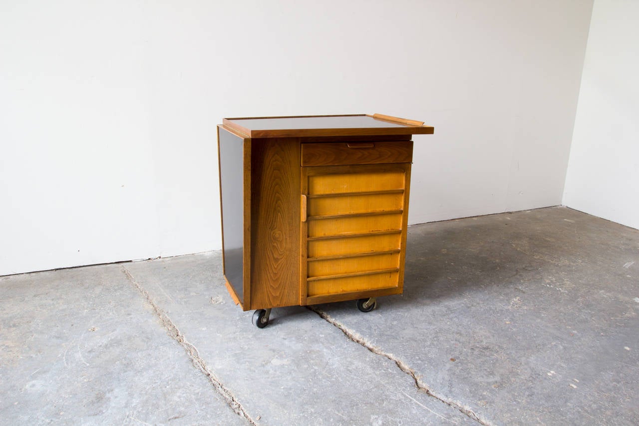 A multifunctional walnut bar cart on casters by Edward Wormley for Dunbar– Model 5433. The cabinet has two cedar shelves which can be adjusted up or down. One drawer above the cabinet provides extra storage for mixing equipment. The laminate