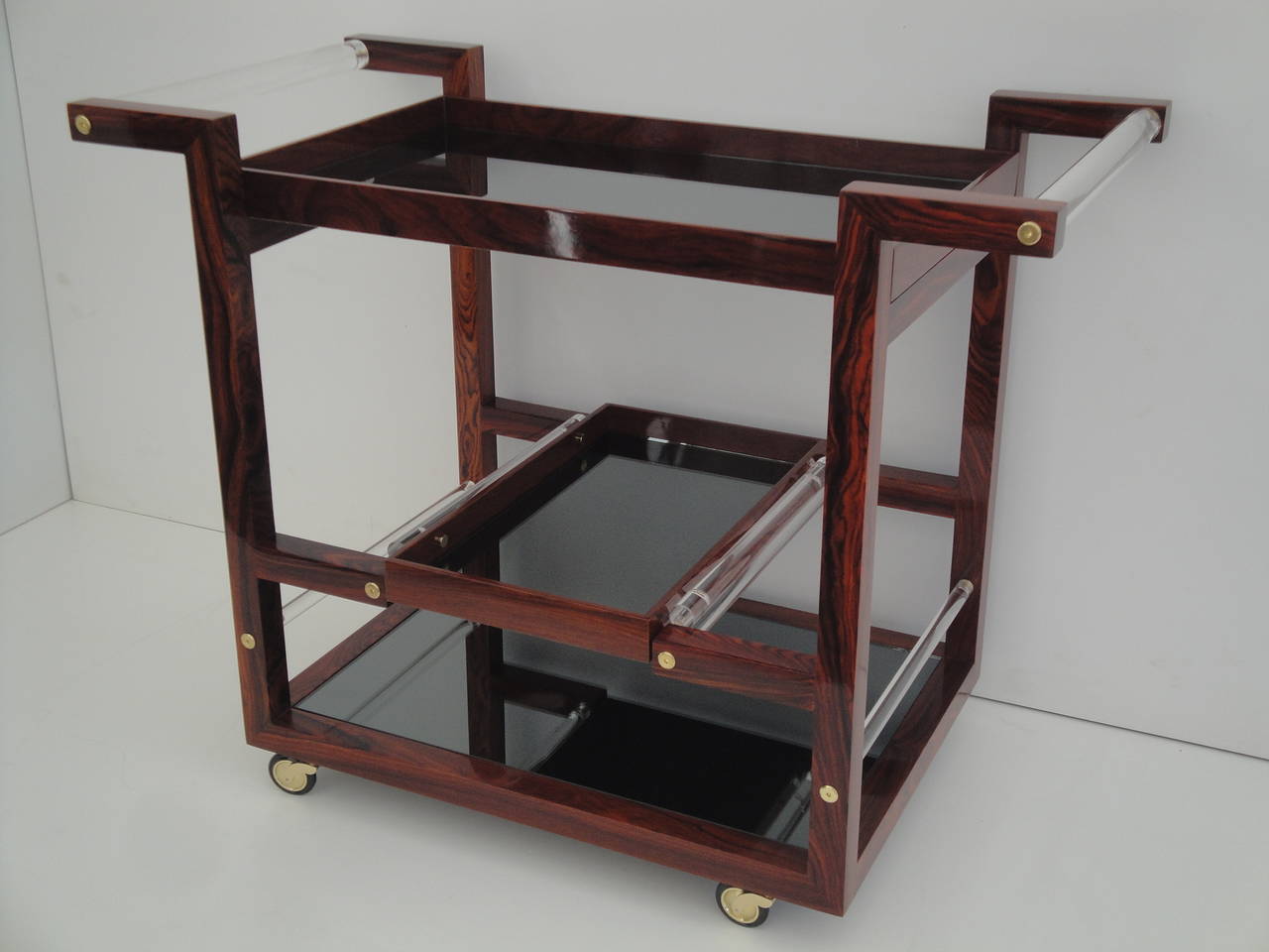 Gorgeous Art Deco style solid rosewood rolling bar cart with Lucite handles and smoke grey mirror shelves and removable tray.