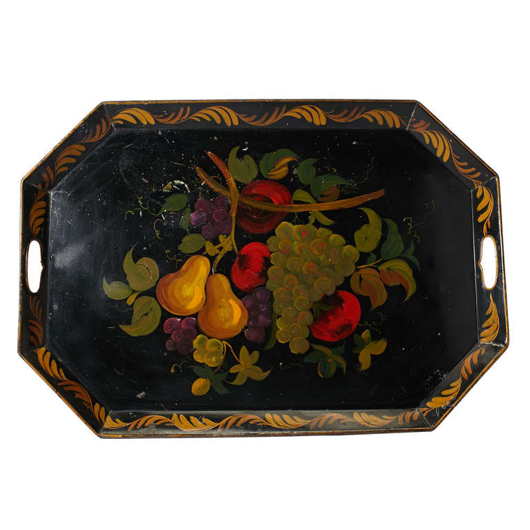 A tole painted tray in an octagon shape with canted sides and two openings for handling, decorated with a group of fruit painted to the center on a black ground.  American, circa 1900.
