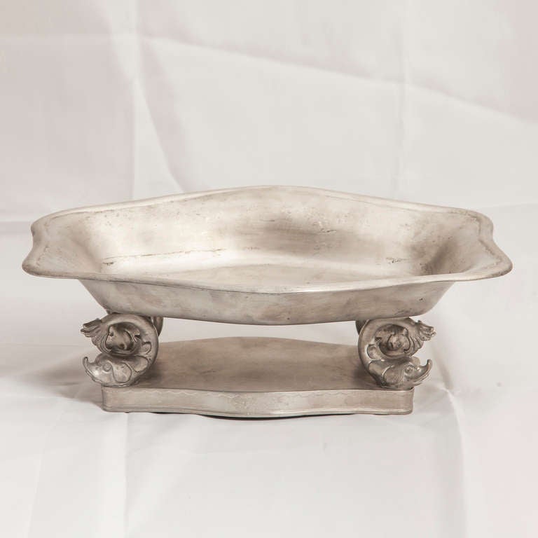 The pewter bowl is supported by 4 dolphins on a pewter base. 
The base is inscribed with 