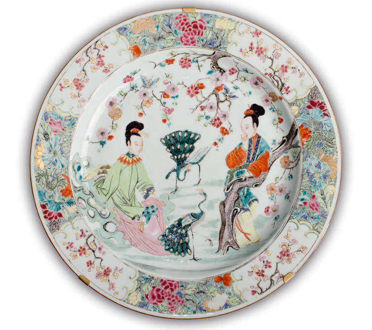 Decorated in famille rose enamels, two ladies, one sitting on rocks, the other leaning against a tree with two peacocks under a branch of flowering blossom, the rim with four cartouches with branches of blossom against a ground of various flowers,