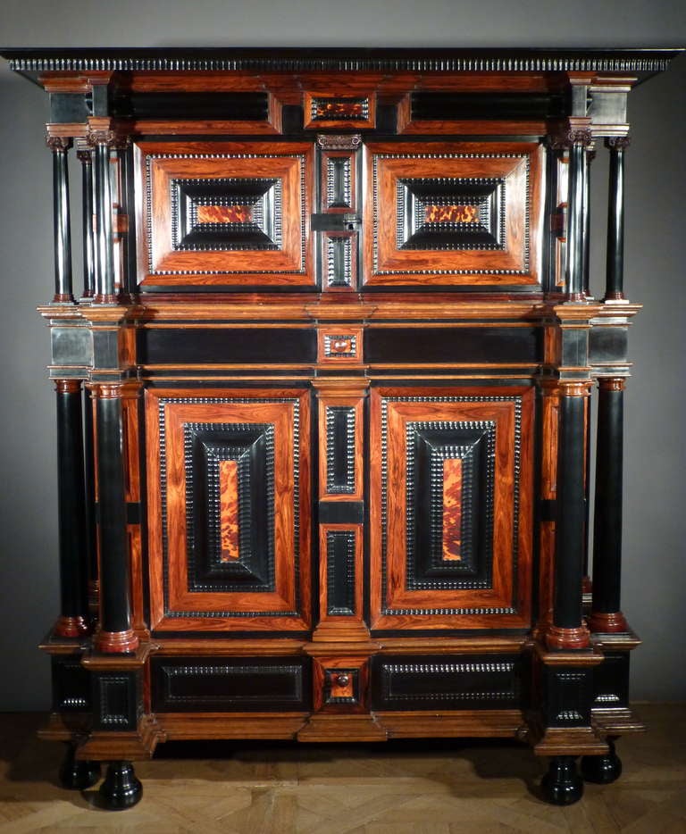 The oversailing cornice  above a pair of panelled doors enclosing an interior with two shelves flanked by six massive tapering ebony columns with carved Corinthian capitals. Below a pair of conforming doors, the raised panels veneered with rosewood