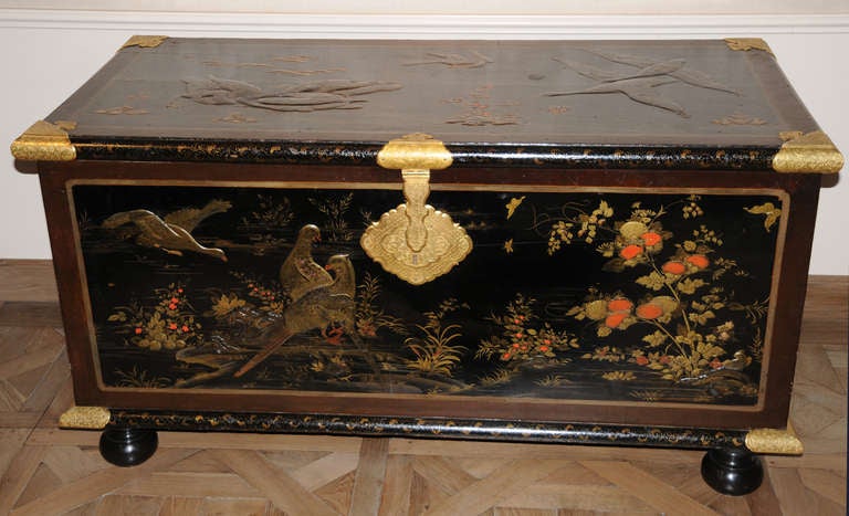 A very unusual European wooden lacquer rectangular chest with flat hinged lid and gilt bronze mounts. Decorated overall in pictorial-style in gold and cinnabar on a black background.  Partially in relief with framed panels of a pond, flowering