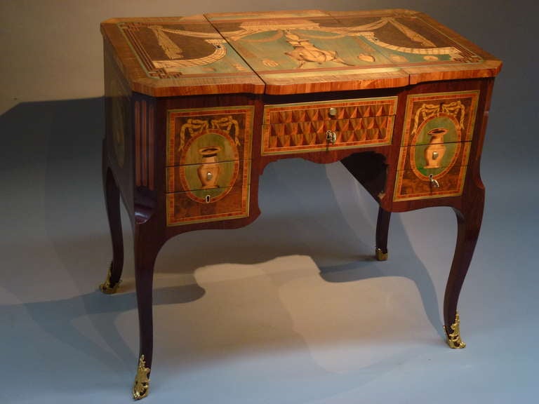 Rectangular top with canted corners with a marquetry of a bust on a vase-shaped stand flaked by various urns and jugs below a lambrequin and drapery. The hinged central  panel top enclosing an easled toilet mirror and flanked to each side by a