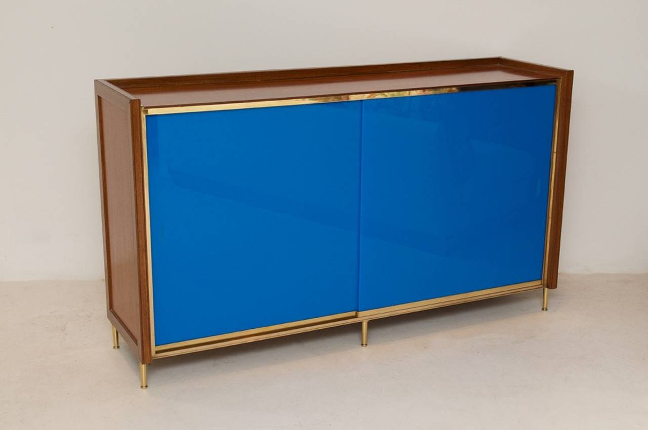 Unusual cabinet in walnut with brass legs and detail and sliding blue acrylic doors. The interior has two shelves.