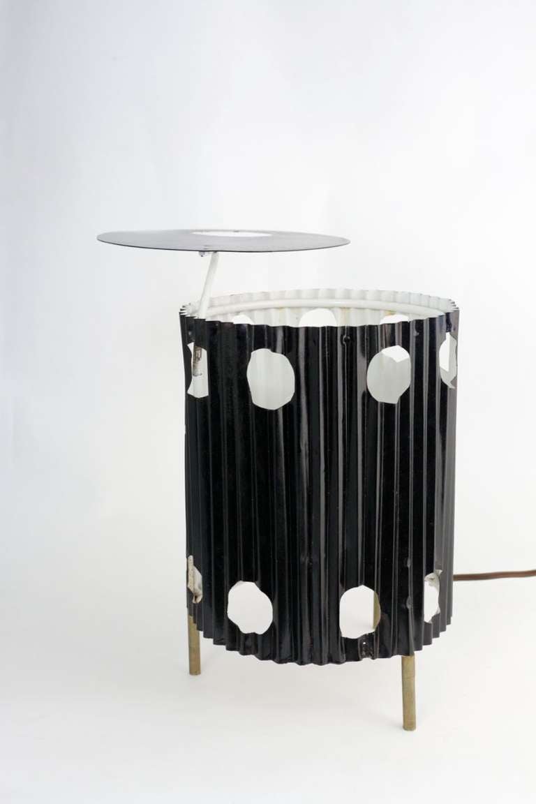 'Java' Table Lamp with a metal structure, original folded steel sheet, white lacquered inside, black lacquered outside, two rows of circled holes on the trunk, tripod brass feet, top reflector made of a circular disk with an asymmetrical hole.