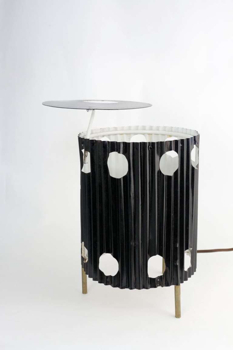 lampe de table 'Java' à structure métallique:: tôle d'acier pliée d'origine:: intérieur laqué blanc:: extérieur laqué noir:: deux rangées de trous circulaires sur le tronc:: pieds tripodes en laiton:: réflecteur supérieur constitué d'un disque