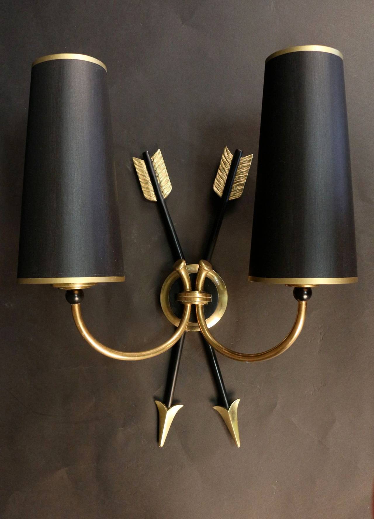 Pair of 1950's 'Arrow' sconces by Maison Arlus in gold and blackened brass. Two crossed arrows on the center-based medallion. Two light arms per sconce, custom redone lampshades, black exterior, gold interior.